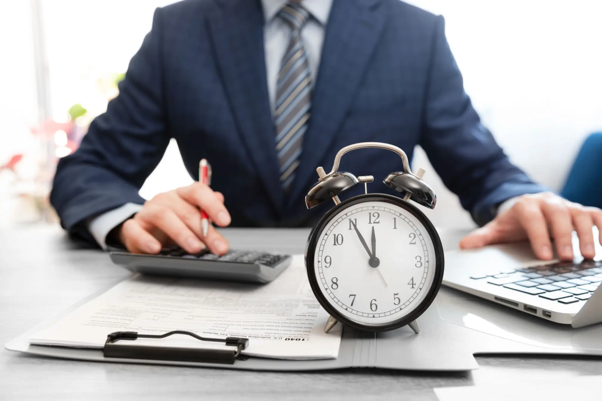 Businessman calculating finances with an alarm clock on the desk.