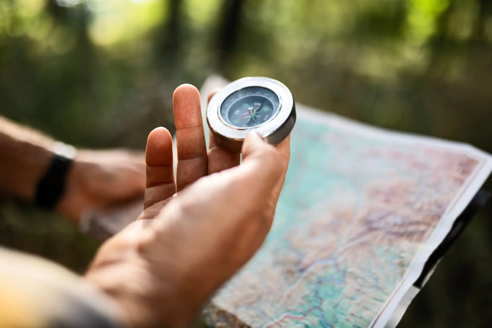 Hand holding a compass over a map outdoors.