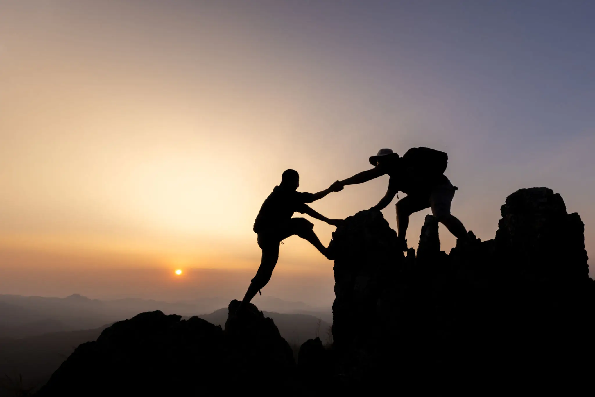 Two climbers helping each other at sunset on a mountain.