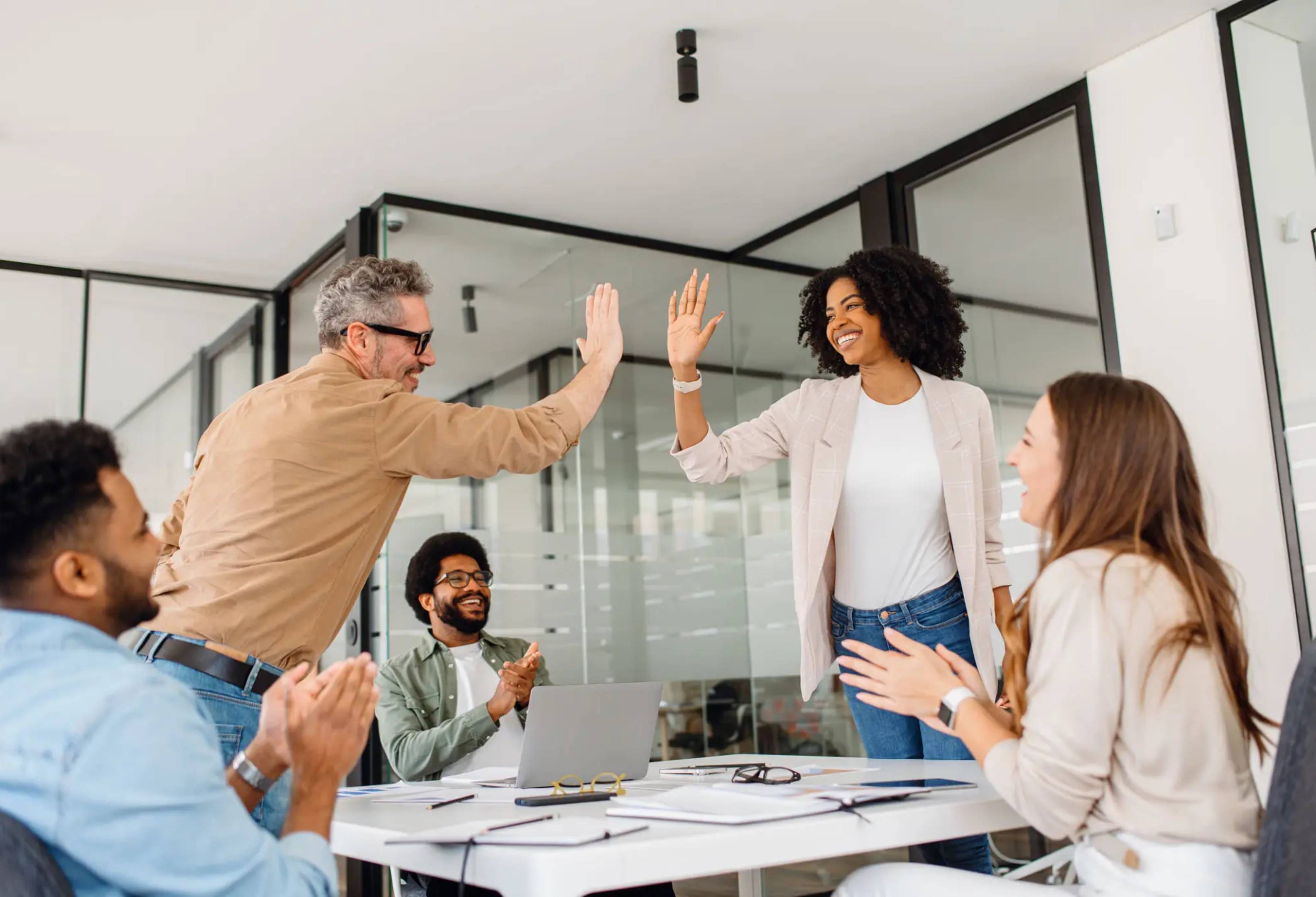 Colleagues celebrating success with high-fives in a modern office.