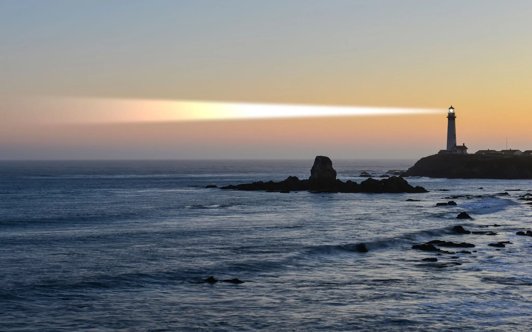 Sunset over a calm sea with rocky formations on the horizon.