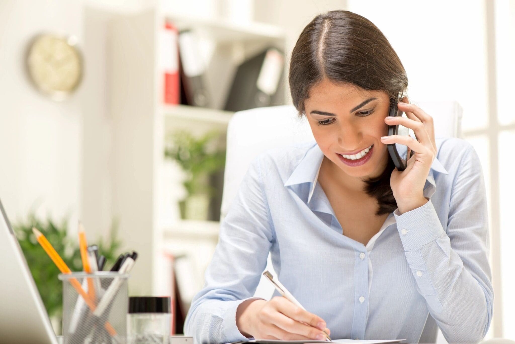 Woman talking on phone while writing notes.