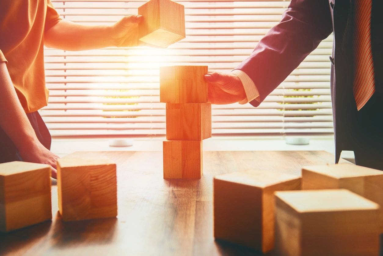 People stacking wooden blocks in sunlight.