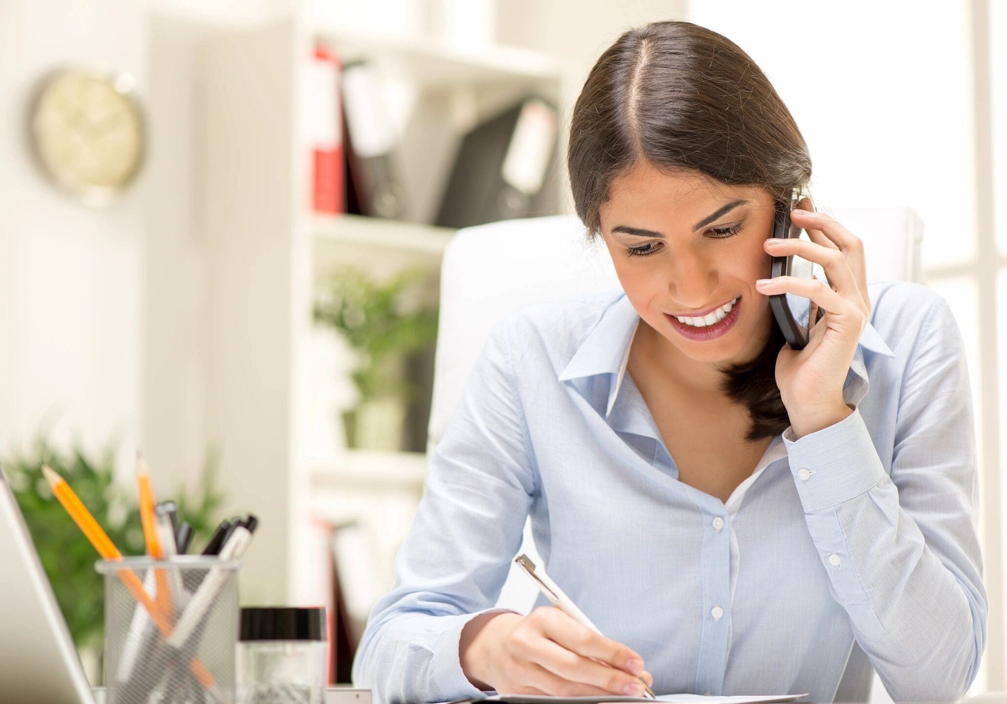 Woman talking on phone while writing notes.