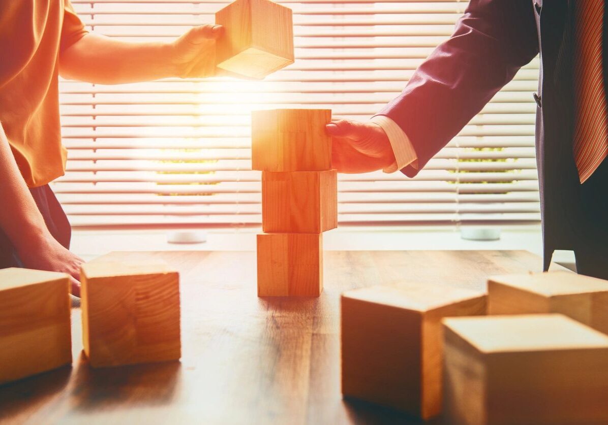 People stacking wooden blocks in sunlight.